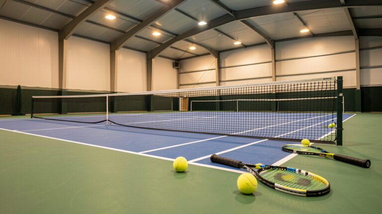 Court de tennis intérieur moderne avec filet, raquettes et balles sous un éclairage chaleureux