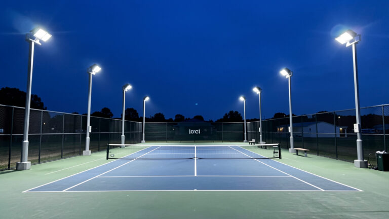 Court de tennis extérieur éclairé par des projecteurs LED modernes au crépuscule.